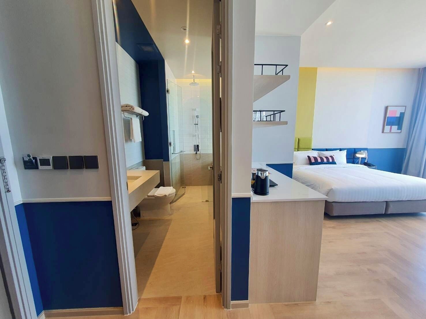 Una habitación de hotel moderna con una cama grande, baño independiente y una pequeña zona de kitchenette.