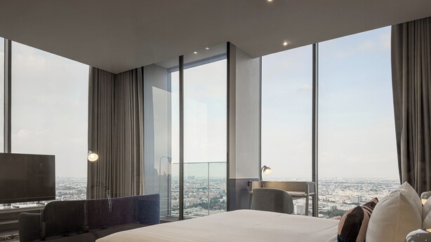 Ein modernes Hotelzimmer mit einem großen Bett, zwei Sesseln, einem Fernseher und Blick auf die Stadt.