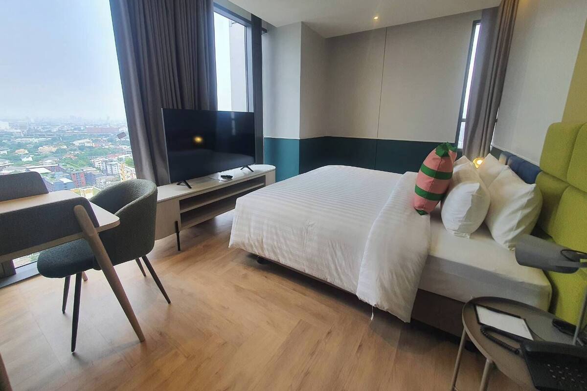 Une chambre d’hôtel avec un lit, un bureau, une chaise, une télévision et une vue sur la ville.