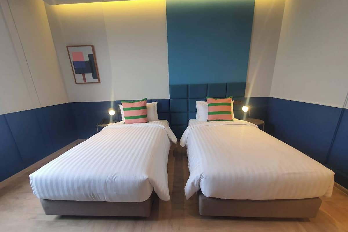 Une chambre d’hôtel avec deux lits, un mur d’accent bleu et un petit tableau accroché au mur.
