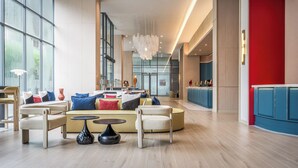 Eine geräumige Lobby mit einer modernen Lounge, einem zentralen Kronleuchter und Blick zum Küchenbereich.