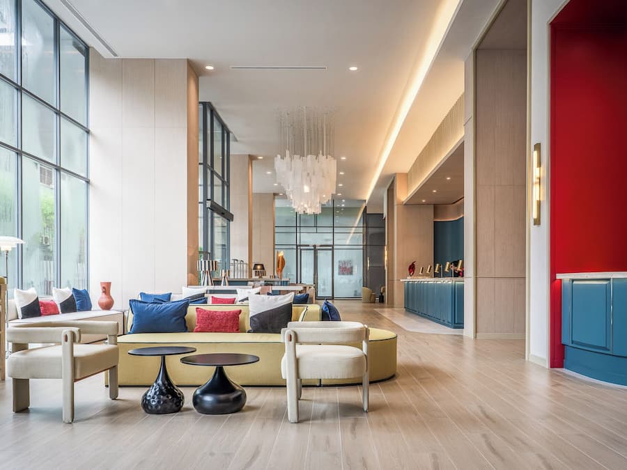 A spacious lobby with a modern seating area, a central chandelier, and a view of the kitchen area.