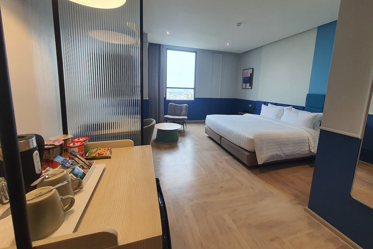 Une chambre d’hôtel comprenant un lit, un bureau avec une machine à café, une chaise et une fenêtre donnant sur la ville.
