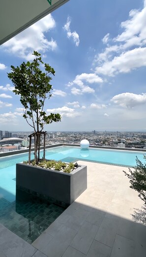 Una piscina infinita en la azotea con vistas despejadas al horizonte urbano, una gran escultura esférica blanca y un macetero con follaje.