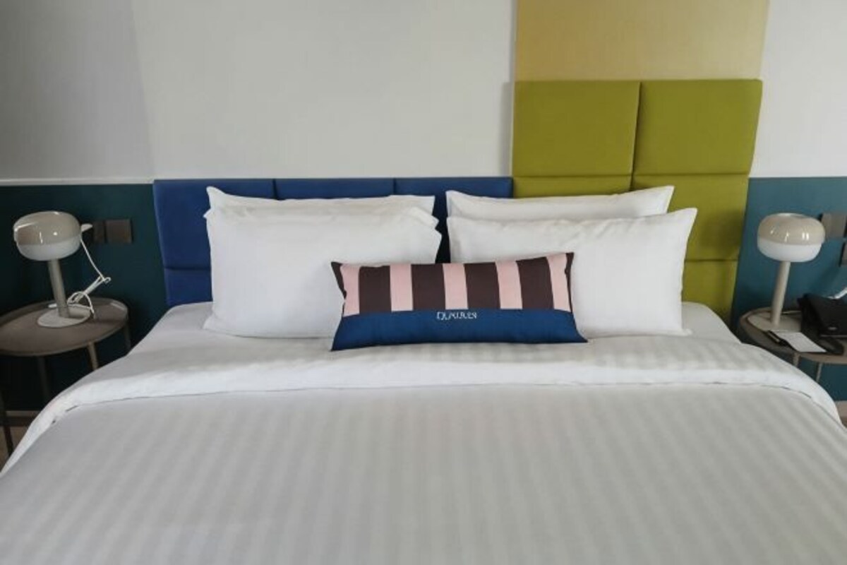 A neatly made bed with white bedding and a blue headboard, two bedside lamps, and a striped pillow.