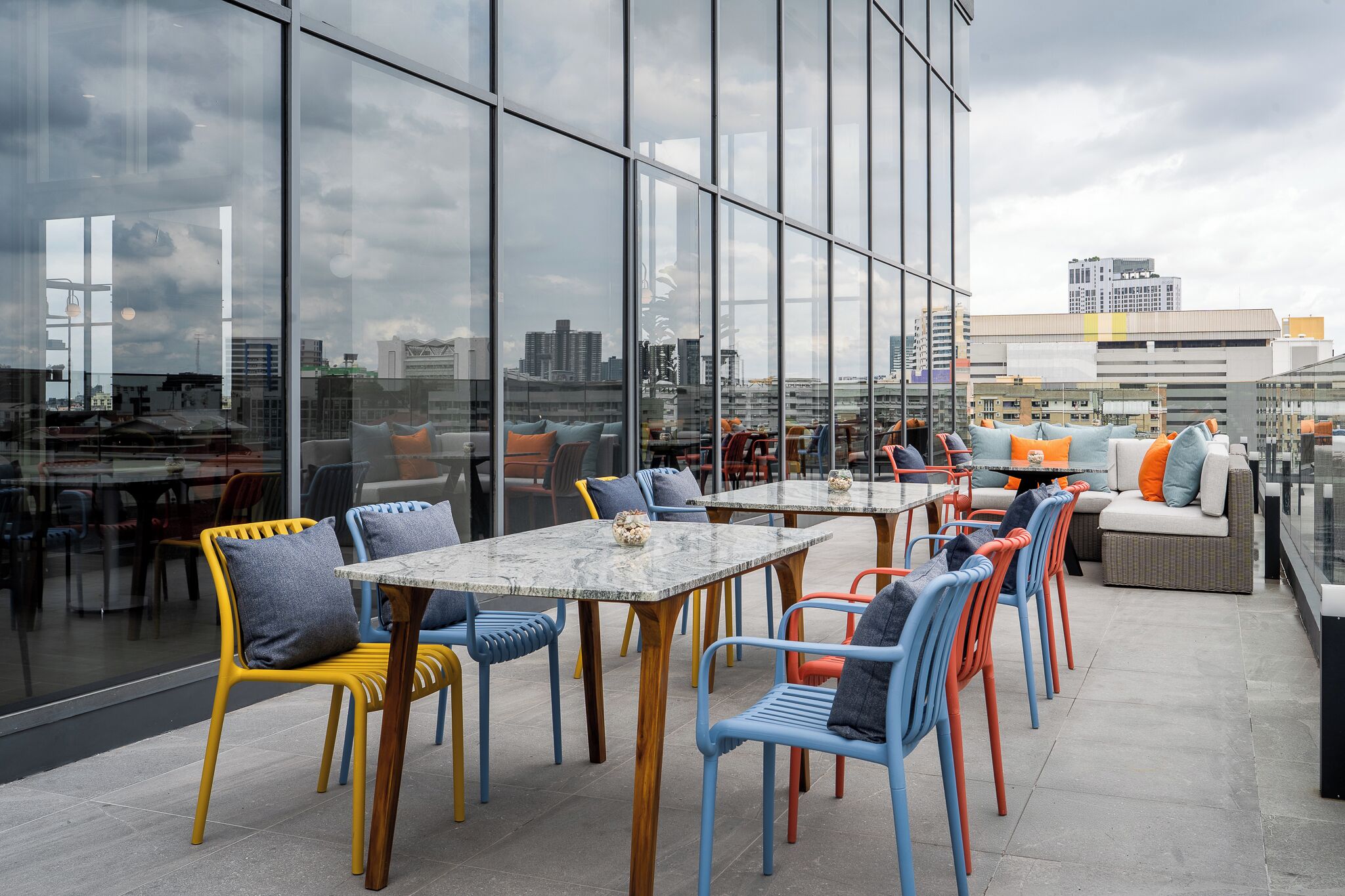 Un espacio exterior con mesas y sillas, ventanas amplias y vistas a la ciudad.