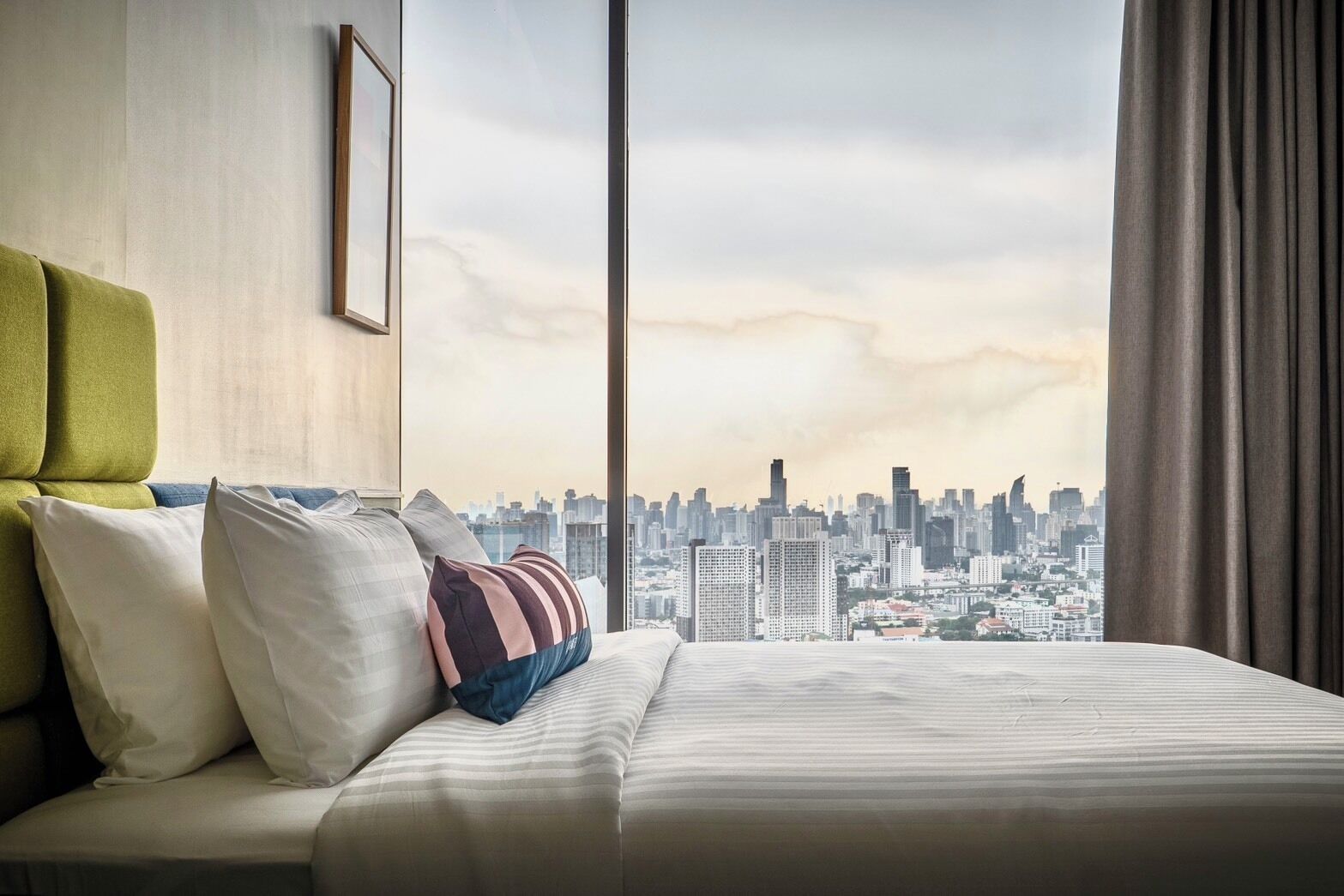 A hotel room with a large bed, a city view, and a window with curtains.