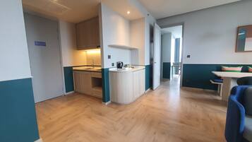 A compact kitchen with a sink, cabinets, and a coffee maker. There is a dining area with a table and chairs.