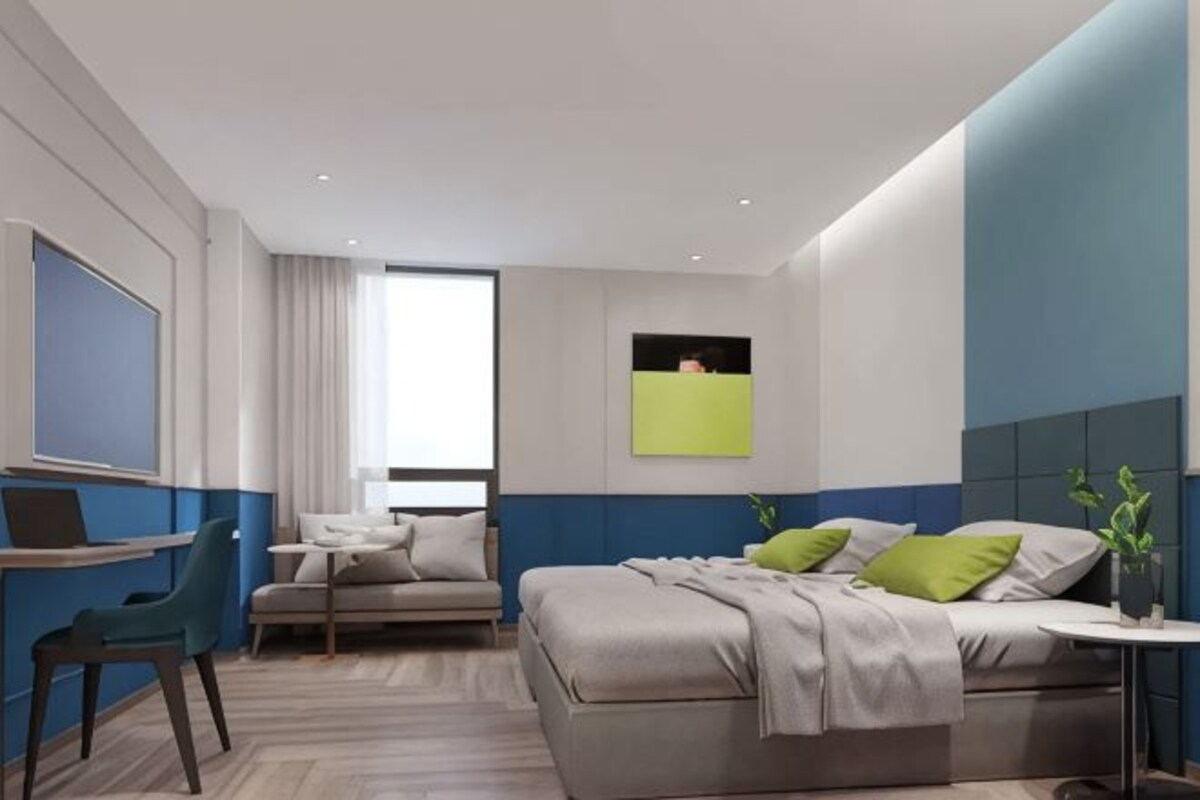 A modern hotel room with a bed, a desk, a chair, a window, and a green plant.