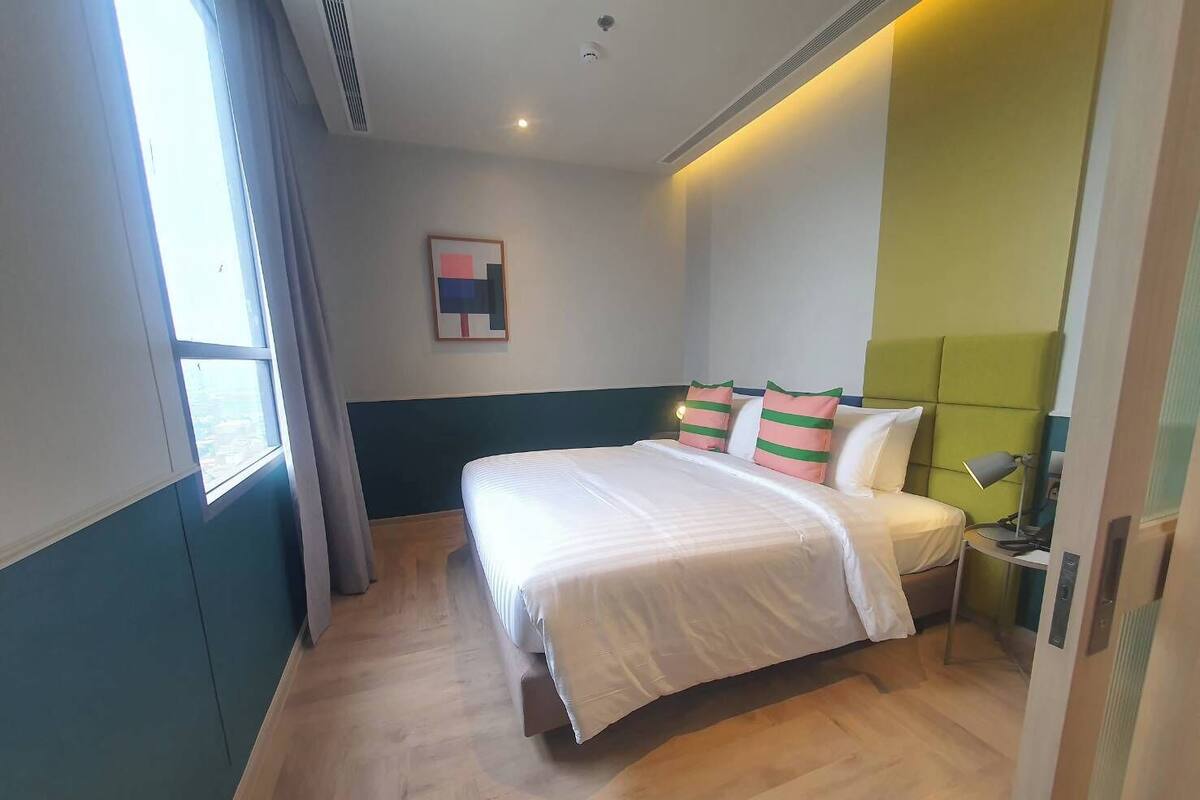 Une chambre d’hôtel avec un lit, une table de chevet, une lampe et une fenêtre avec des rideaux.