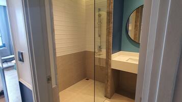 A modern bathroom with a glass shower enclosure, a sink with a mirror, and a tiled floor.