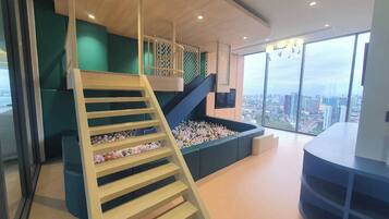 A modern interior with a wooden staircase, a ball pit, and a city view through large windows.