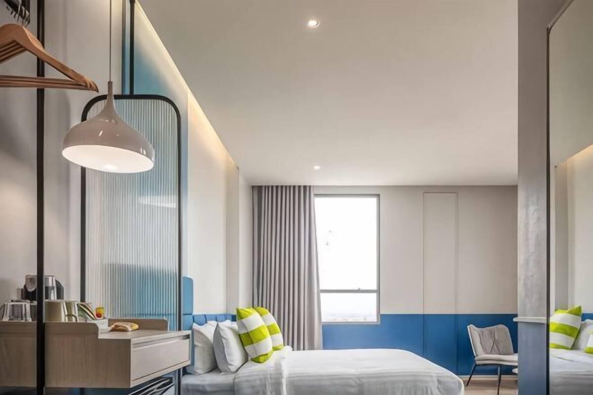 Une chambre d  ’hôtel moderne, équipée d’un lit, d’une table de chevet, d’une lampe et d’une grande fenêtre.