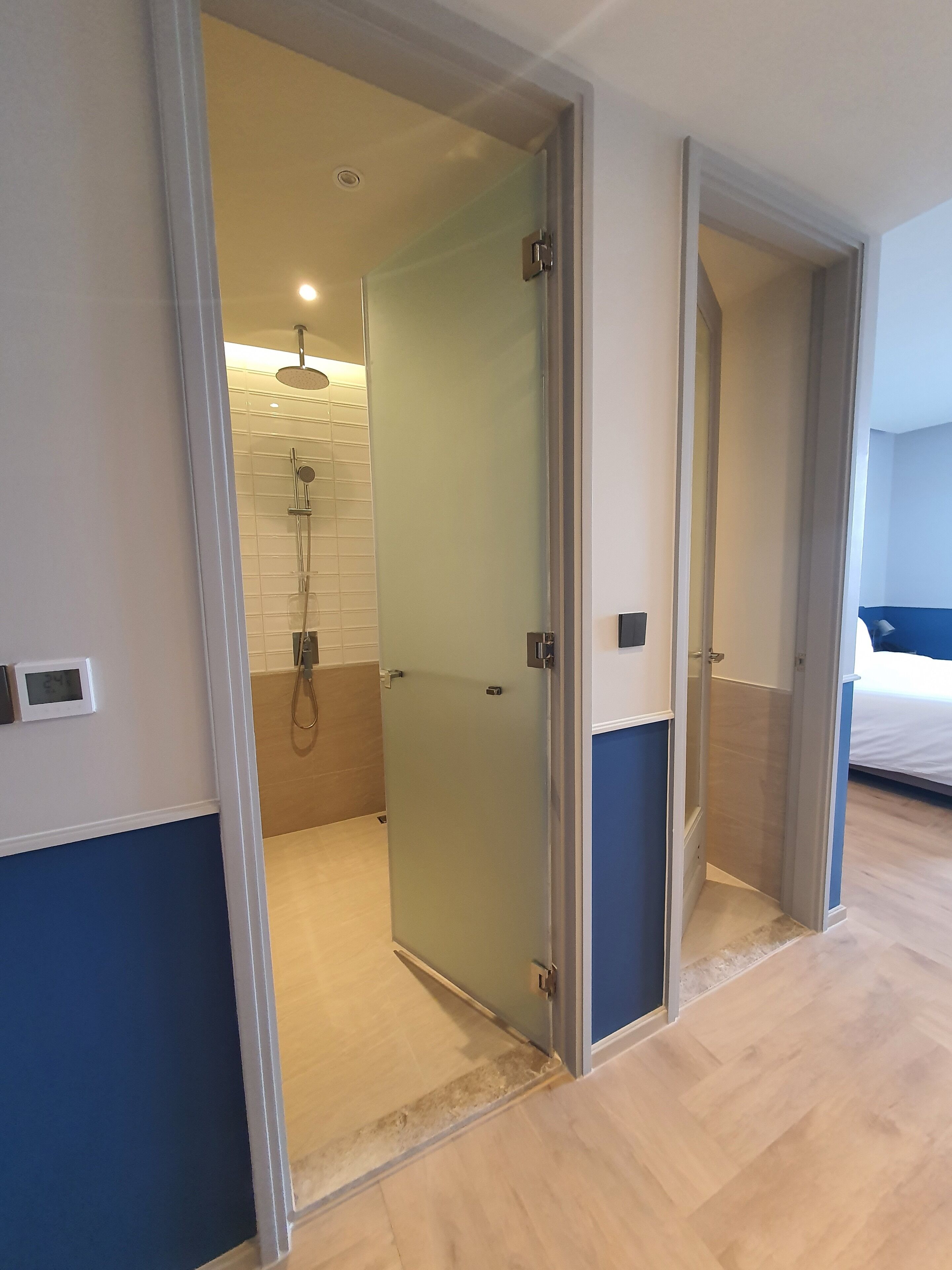 A modern bathroom with a glass shower enclosure, a visible showerhead, and a digital thermostat on the wall.
