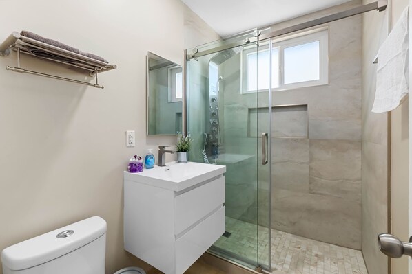 Un baño moderno con ducha envuelta en vidrio, tocador blanco con lavamanos y un inodoro.