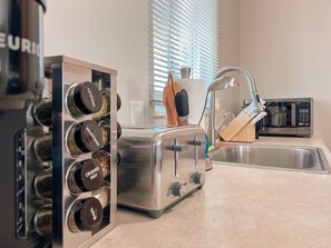 A kitchen with a toaster, a sink, a microwave, and a spice rack.