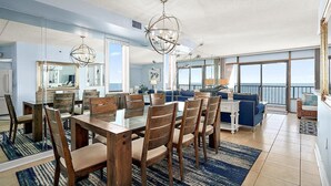 Een ruime eethoek met een grote tafel en stoelen, een balkon met uitzicht en een moderne kroonluchter.