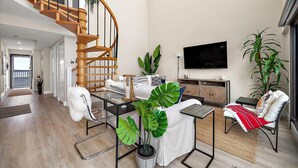 Ein modernes Wohnzimmer mit einer Wendeltreppe aus Holz, einem Flachbildfernseher und mehreren Pflanzen.