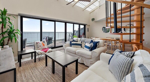 A spacious living area with a large window overlooking the sea, a wooden staircase, and a dining area. - 2 Bedroom Penthouse with Oceanfront Views! (Ocean City)
