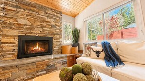 A cozy living room with a stone fireplace, a sofa, a coffee table with decorative items, and a window with a view of trees. - Tahoe Retreat AC Hot Tub Backyard Oasis, Near Skiing & Beaches (SL397) (Stateline)