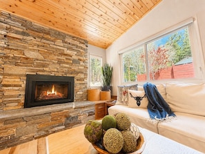 A cozy living room with a stone fireplace, a sofa, a coffee table with decorative items, and a window with a view of trees. - Tahoe Retreat w/ AC | Hot Tub+Backyard Oasis | Near Skiing & Beaches (SL397) (Stateline)