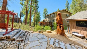 A wooden deck with stone tiles, a red pergola, and a large tree stump sculpture. - Tahoe Retreat AC Hot Tub Backyard Oasis, Near Skiing & Beaches (SL397) (Stateline)