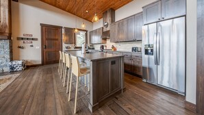 A modern kitchen with wooden flooring, a central island with bar stools, stainless steel appliances, and a stone fireplace. - Treehouse at the Wilderness Club (Eureka)