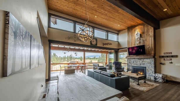 A spacious living area with a large wooden table, comfortable seating, a stone fireplace, and a scenic view through large windows. - Treehouse at the Wilderness Club (Eureka)