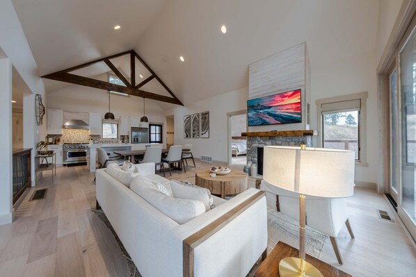 A spacious living room with a white sofa, a wooden coffee table, and a fireplace. There is a kitchen in the background with modern appliances and a dining area. - Wilderness Club Haven for 12! (Eureka)