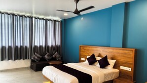 A modern bedroom with a wooden headboard, a bed with white and black bedding, a bedside table, a nightstand, a ceiling fan, and a window with curtains. - Mount Minar (Devikolam)