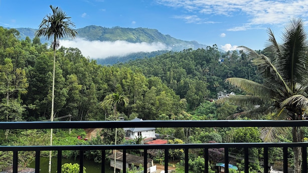 A lush green landscape with a river, a house, and a mountain range in the background. - Mount Minar (Devikolam)