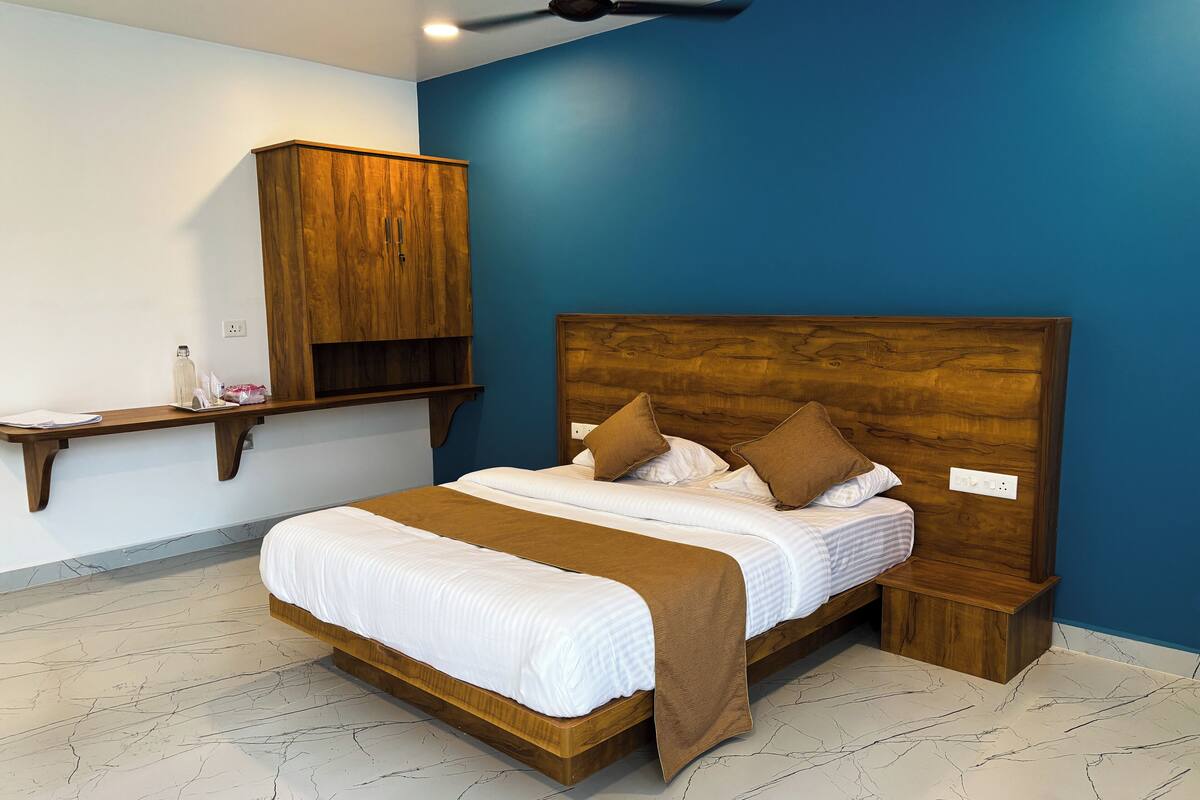A bedroom with a wooden headboard, a bed with white bedding and brown pillows, a wooden nightstand, and a shelf with toiletries.
