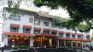 A multi-story building with a white facade and red-tiled roofs, featuring large windows and a covered entrance area. - NO 18 HOTEL (Kochi)
