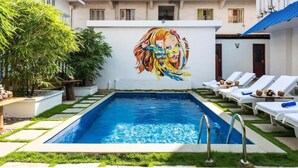 A swimming pool with lounge chairs, a mural, and a building in the background. - NO 18 HOTEL (Kochi)