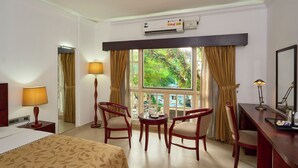 A hotel room with a bed, two chairs, a small table, a desk, a mirror, and a large window with curtains. - NO 18 HOTEL (Kochi)