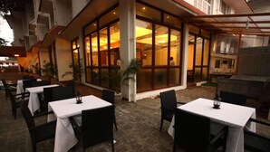 An outdoor dining area with tables and chairs, a large glass window, and a building with a tiled roof. - NO 18 HOTEL (Kochi)
