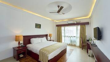 A hotel room with a bed, bedside lamps, a desk with a computer, a ceiling fan, and an air conditioning unit.
