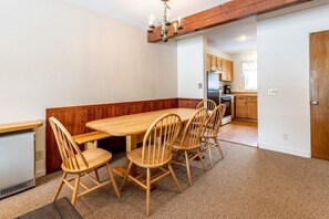 Ein Essbereich mit einem Holztisch und Stühlen, im Hintergrund eine Küche und ein Holzbalken an der Decke.