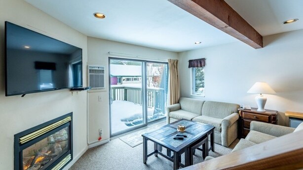 Een woonkamer met een open haard, een televisie, een bank, een salontafel en een balkon met een schuifdeur.