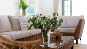 A living room with a white sofa, a glass coffee table with a vase of flowers, and a wicker chair. - Gibbs Glade Villa 4 Bedroom Home by Bluescape (Gibbes)