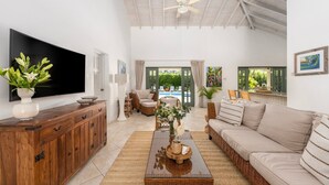 A spacious living room with a large flat-screen TV, a wooden cabinet, a beige sofa, and a wicker coffee table. - Gibbs Glade Villa 4 Bedroom Home by Bluescape (Gibbes)
