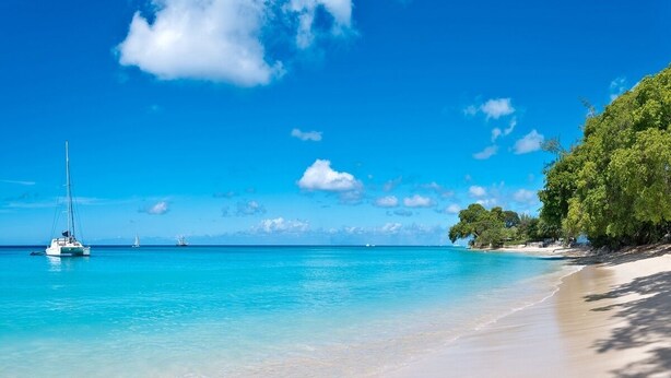 A beach with clear turquoise water, a sailboat, and a tree-lined shore. - Gibbs Glade Villa 4 Bedroom Home by Bluescape (Gibbes)