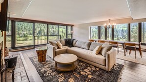 A modern living room with a large sectional sofa, a round coffee table, and a dining area with a wooden table and chairs. - 1776 Decatur 4 Bedroom Condo (Keystone)