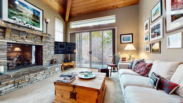 A cozy living room with a stone fireplace, a flat-screen TV, and a large window offering a view of the outdoors. - Snowcreek Iv #545 3 Bedroom Condo (Mammoth Lakes)
