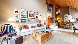 A cozy living room with a white sofa, a wooden coffee table, and a collection of framed pictures on the wall. - Snowcreek Iv #545 3 Bedroom Condo (Mammoth Lakes)