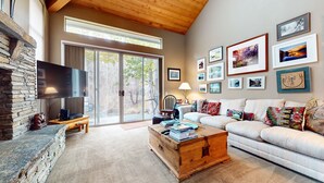 A cozy living room with a stone fireplace, a flat-screen TV, a wooden coffee table, and a sofa with colorful cushions. - Snowcreek Iv #545 3 Bedroom Condo (Mammoth Lakes)