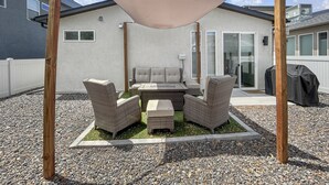 Een terras met een zithoek, bestaande uit een bank en twee stoelen, onder een beschaduwd dak.