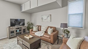 A living room with a brown leather sofa, a coffee table, a TV on a cabinet, and a window with blinds. - The Loft Of Historic Charm 1 Bedroom Condo (Grand Junction)