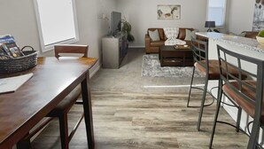 A modern kitchen with a dining area, a living room with a sofa and coffee table, and a kitchen island with bar stools. - The Loft Of Historic Charm 1 Bedroom Condo (Grand Junction)