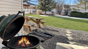 A grill with tongs and a fire, a picnic table, and a grassy yard with a fence. - Hermosa Haven 3 Bedroom Home (Montrose)